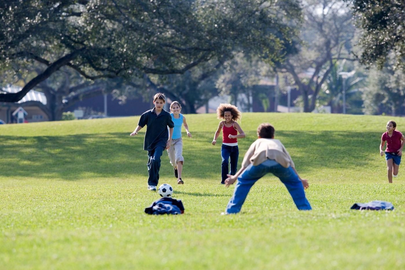 Children running after a soccer ball in a sunny park