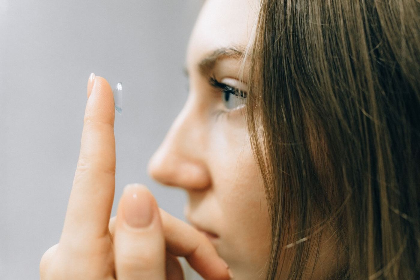 A young woman holding a soft contact lens on her fingertip